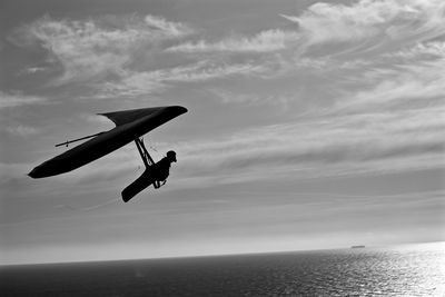 Silhouette man hang-gliding above sea