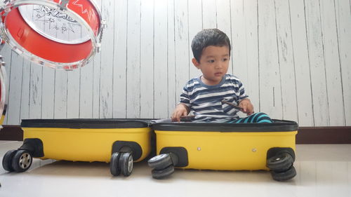 Cute boy sitting in luggage by drums at home