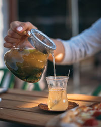 Midsection of person pouring drink in glass on table