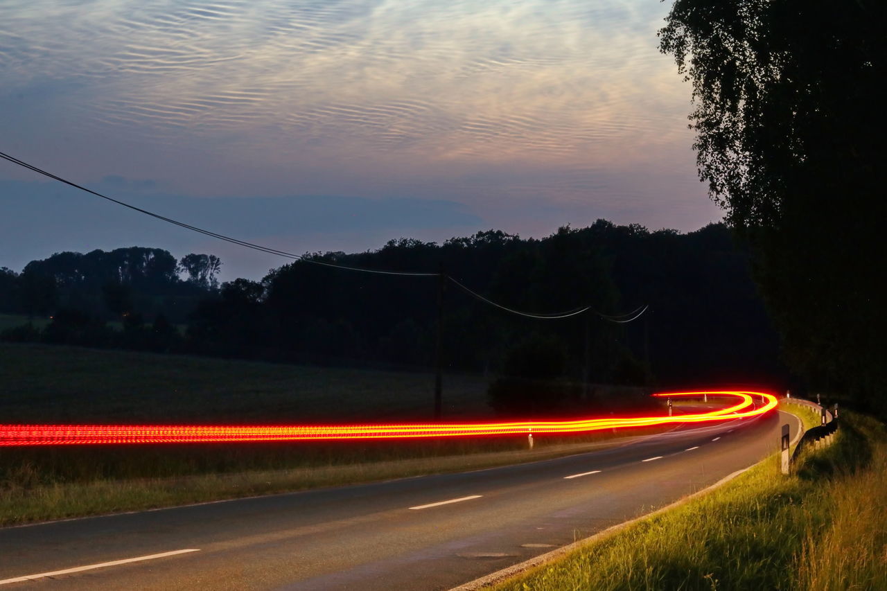 LIGHT TRAILS ON STREET AGAINST SKY DURING SUNSET