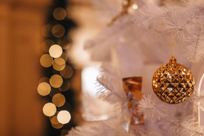 Golden christmas ball hanging on the white christmas tree. magic golden bokeh lights