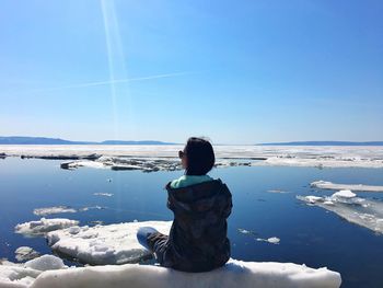 Rear view of woman sitting on ice in sea against blue sky