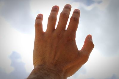 Cropped hand gesturing against sky