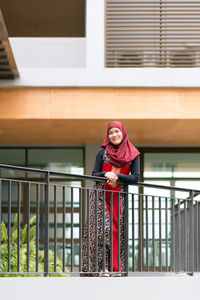 Portrait of smiling woman in hijab standing at balcony