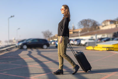 Young woman walking with suitcase on parking lot