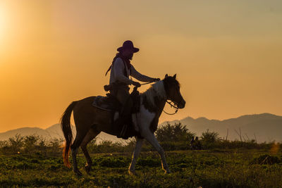 Man riding horse on field against sky during sunset