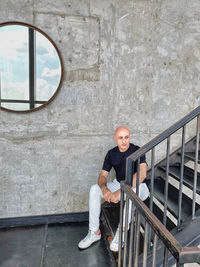 Portrait of young man sitting on railing against wall