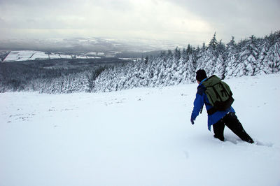 Rear view of hiker with backpack walking in deep snow against sky