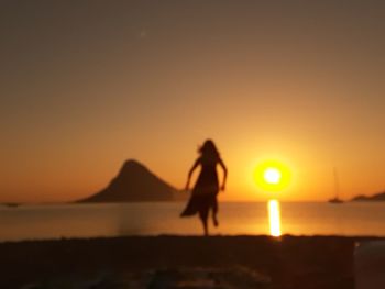 Silhouette woman standing on beach against sky during sunset