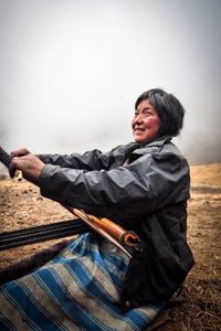 Mature woman working while sitting on field during foggy weather