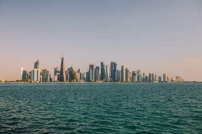 Contemporary skyscrapers located on coast of rippling sea against cloudless sundown sky in evening in doha, qatar