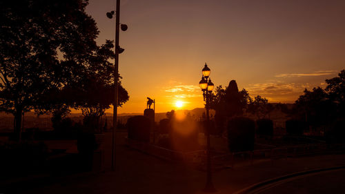 Silhouette trees by street against sky during sunset