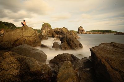 Shirtless man sitting on rock by sea against sky