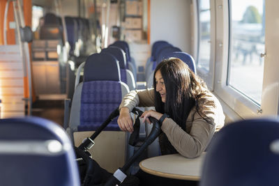 Smiling woman on parental leave in train looking at baby in pram