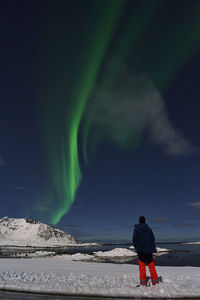 Rear view of man standing on snow watching aurora