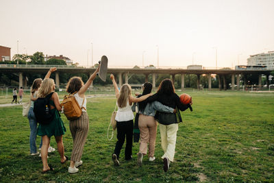 Rear view of teenage girls with hand raised walking by friends at park