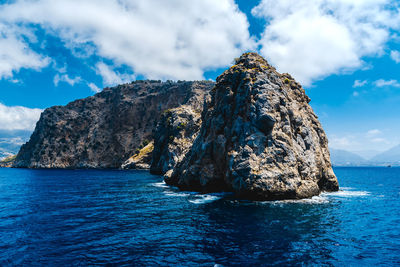 Rock formation in sea against cloudy sky