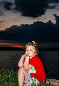 Portrait of woman sitting by lake against sky