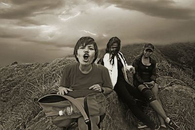 Portrait of friends sitting on field against storm clouds