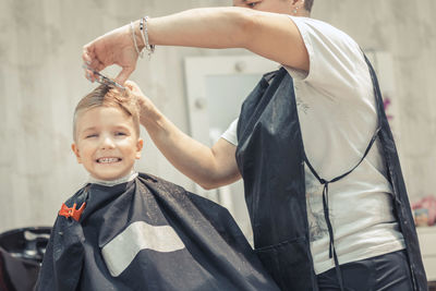 Midsection of barber cutting hair of boy at shop