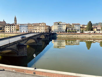 Arch bridge over river by buildings against sky in city