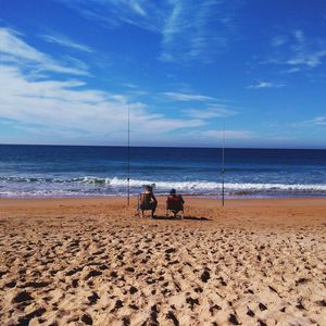 Men sitting on beach against sky