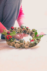 Cropped image of person making wreath on floor in brightly lit room