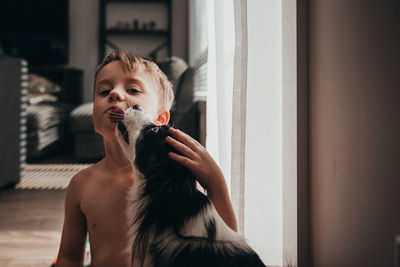 Portrait of shirtless boy kissed by dog at home
