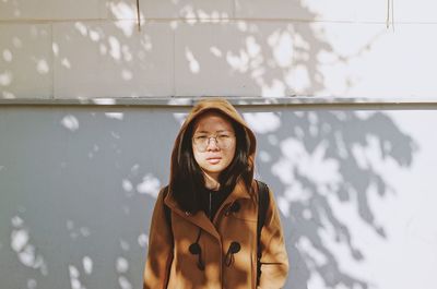 Portrait of young woman standing against wall