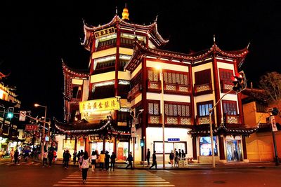 People walking on illuminated street against buildings at night