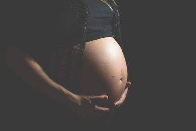 Midsection of pregnant woman against black background