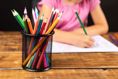 Midsection of girl drawing on paper with colored pencils at table