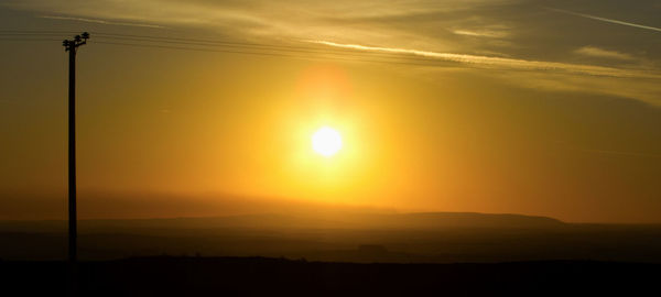 Silhouette electricity pylon against sky during sunset