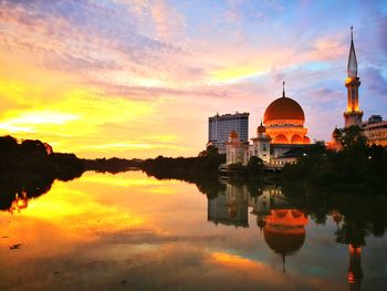 Illuminated mosque by river against sky during sunset