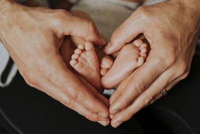 Cropped hands of mother making heart shape by baby feet