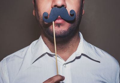 Close-up of man with prop mustache against gray background