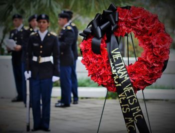 Close-up of red wreath with army soldiers standing in background