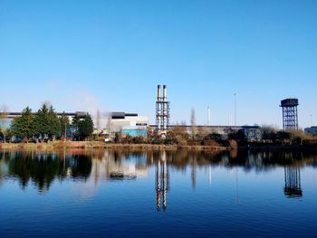 Reflection of buildings in lake against clear blue sky