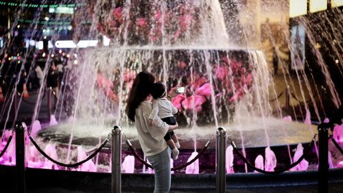 Side view of woman carrying daughter by fountain