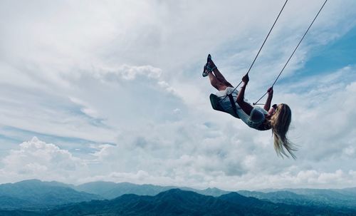 Low angle view of woman on swing against sky