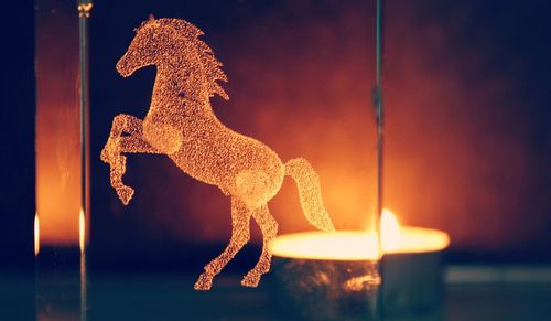 Close-up of horse carved on glass against lit tea light