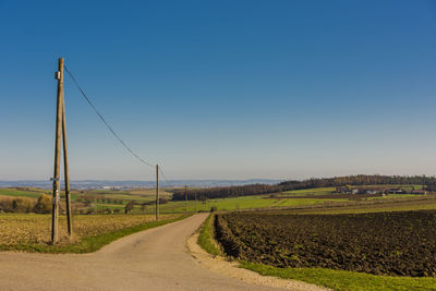 Empty road amidst field against clear blue sky