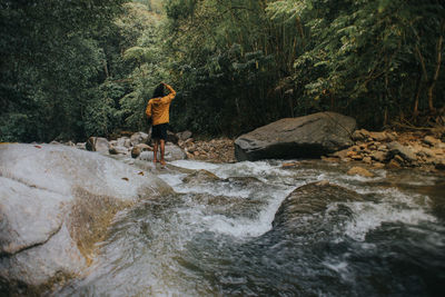 Rear view of man standing on rock by river in forest