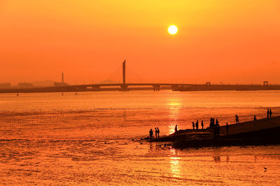 Silhouette bridge over sea against orange sky