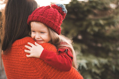 Young woman mom spend time with daughter kid girl wear red knit sweater and hat over tree 