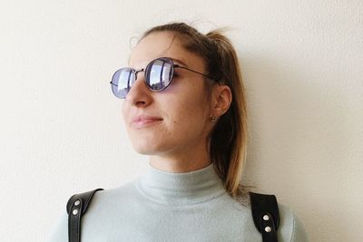 Portrait of young woman wearing eyeglasses against wall