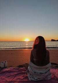 Rear view of woman sitting on beach during sunset