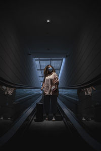 Young woman wearing protective face mask standing on escalator during covid-19