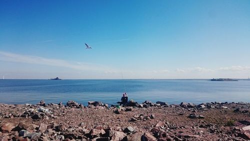 Person sitting on chair next to water for fishing against clear sky