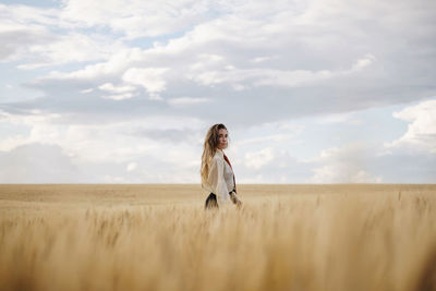 Side view of young mindful female in formal wear with tie looking at camera among spikes in countryside